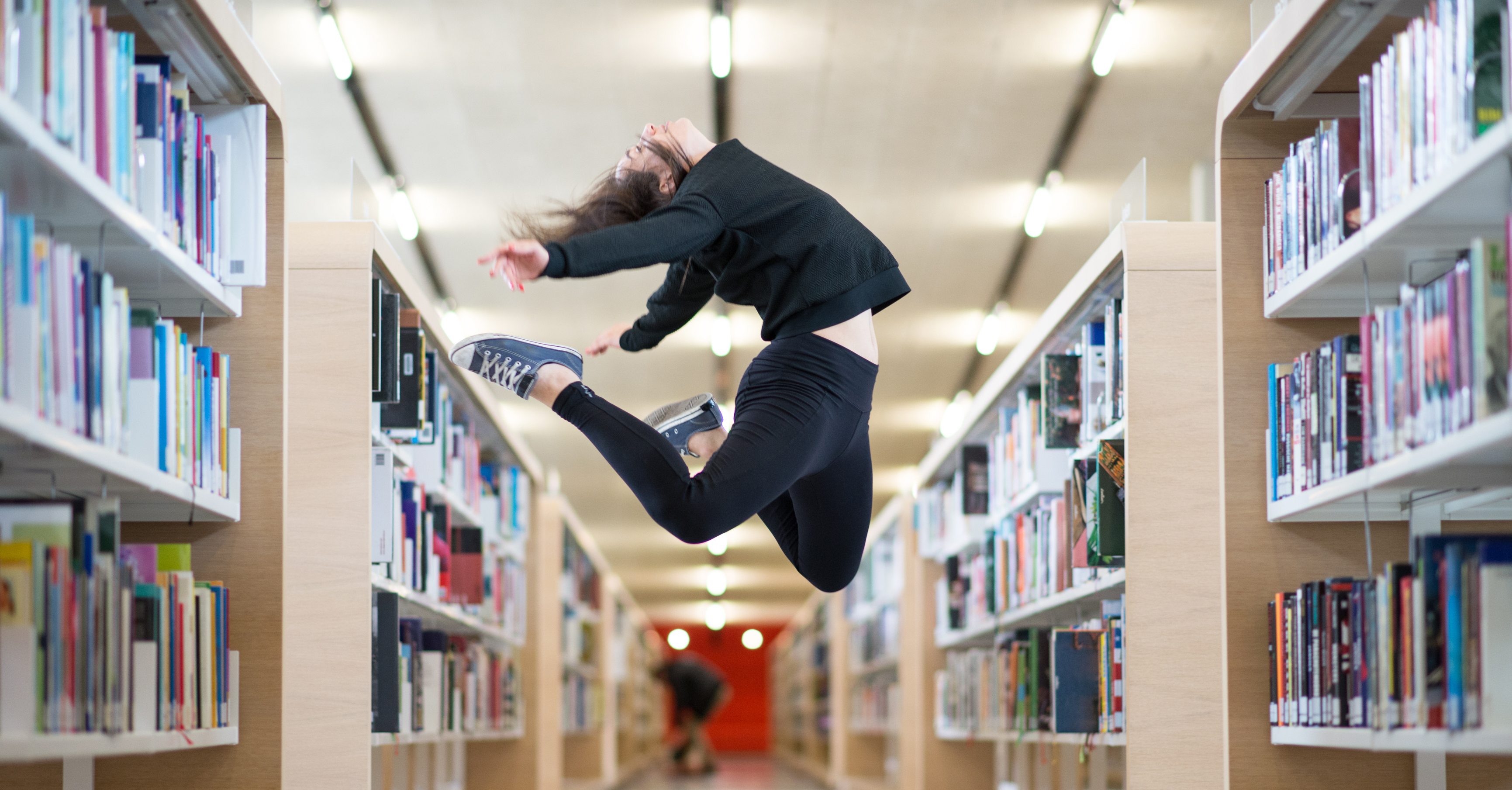 Frau springt zwischen Bücherregalen hoch