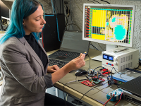 Forscherin sitzt im Labor und hält einen Computerchip in der Hand.