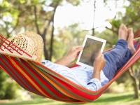 Mann mit Strohhut und Tablet in einer Hängematte liegend