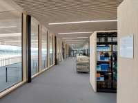 Gang der Teilbibliothek Sport- und Gesundheitswissenschaften Richtung Ausgang mit Regalen und Ausleihtheke rechts und Fensterfront links