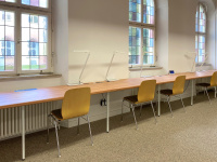 Study desks at a long tabletop in front of windows with stained glass