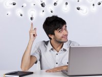 Young man with laptop and notebook who "sees the light". Lots of lightbulbs above his head