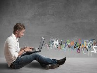 Young man sitting on the ground and letters flying from his laptop