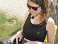 Studentin mit Laptop, Headset und Sonnenbrille draußen im Grünen