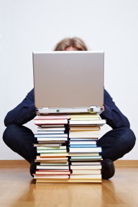 Studentin hinter einem Bücherstapel mit Laptop obendrauf