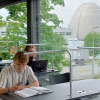 Student sitzt am Lernpaltz mit aufgeschlagenem Buch vor sich und liest etwas am Handy.