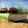 Book and sunglasses in the sand, grass in the background