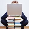 Student behind a pile of books and a notebook on top