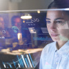 Porträt einer Studentin, während sie auf einen Bildschirm mit Hologrammen schaut, Büroszene im Hintergrundt