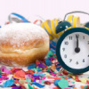 Krapfen mit einer Uhr, die auf 12 steht, Luftschlangen im Hintergrund. Faschingsstimmung.